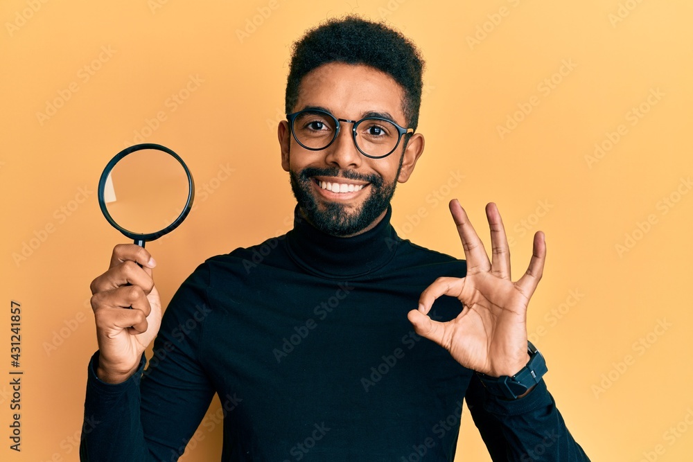 Handsome hispanic man with beard holding magnifying glass doing ok sign with fingers, smiling friendly gesturing excellent symbol Handsome hispanic man with beard holding magnifying glass doing ok sign with fingers, smiling friendly gesturing excellent symbol