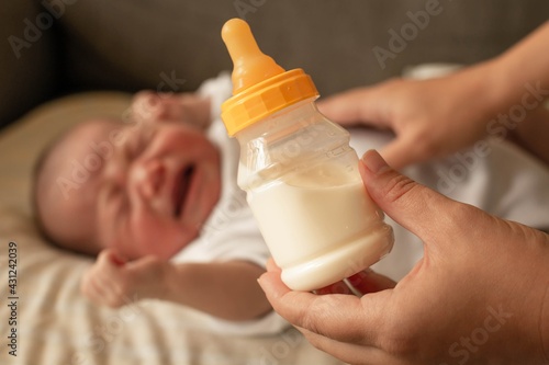 Mother trying to feed her hungry fussy baby with a bottle of milk.