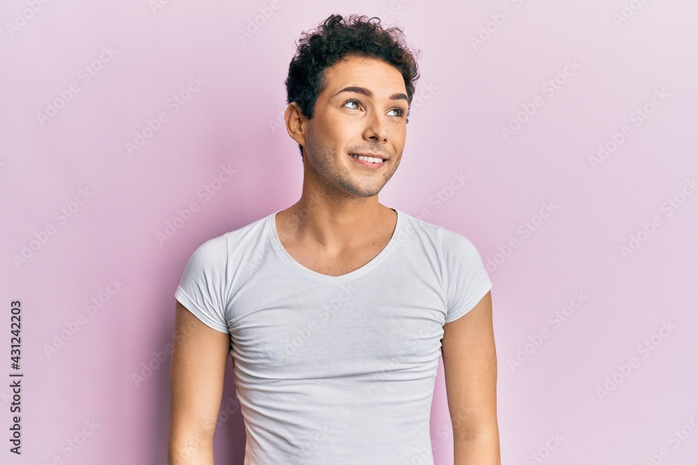 Obraz premium Young handsome man wearing casual white t shirt looking away to side with smile on face, natural expression. laughing confident.