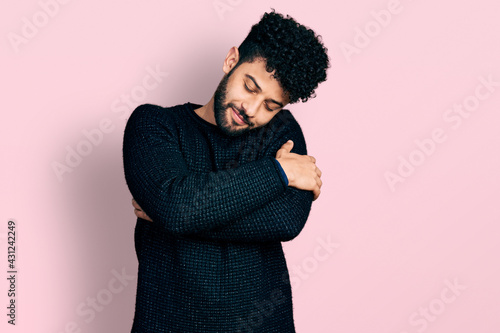 Young arab man with beard wearing casual winter sweater hugging oneself happy and positive, smiling confident. self love and self care © Krakenimages.com