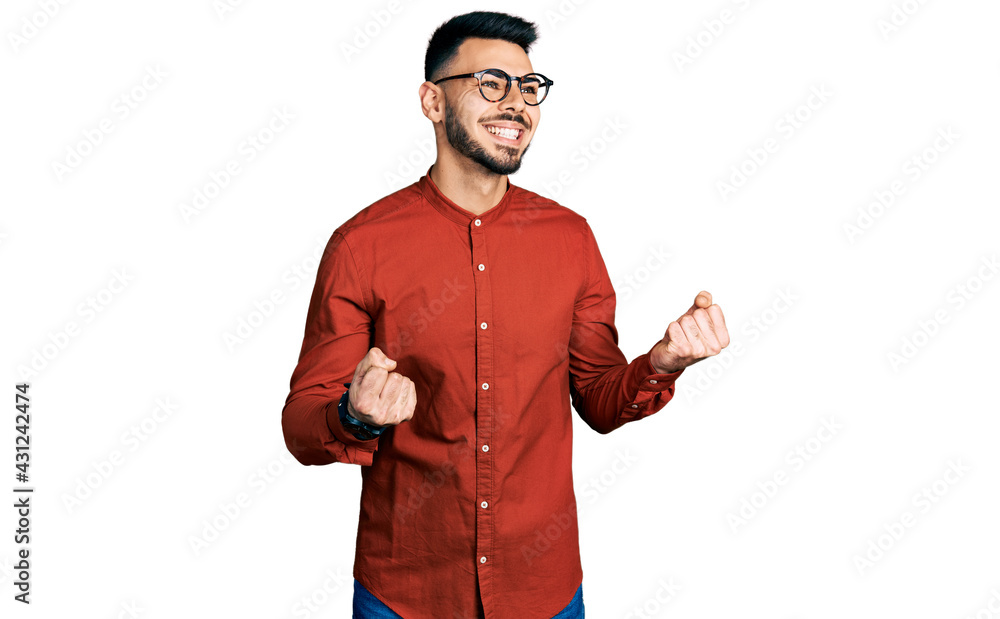 Young hispanic man with beard wearing business shirt and glasses excited for success with arms raised and eyes closed celebrating victory smiling. winner concept. Young hispanic man with beard wearing business shirt and glasses excited for success with arms raised and eyes closed celebrating victory smiling. winner concept.