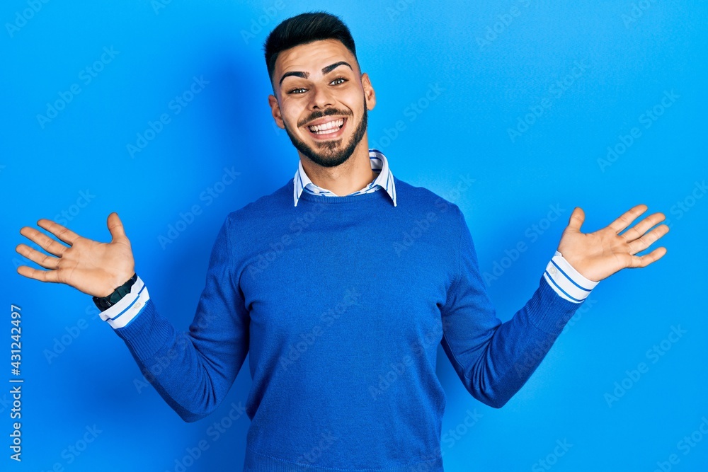 Young hispanic man with beard wearing casual blue sweater celebrating crazy and amazed for success with arms raised and open eyes screaming excited. winner concept Young hispanic man with beard wearing casual blue sweater celebrating crazy and amazed for success with arms raised and open eyes screaming excited. winner concept