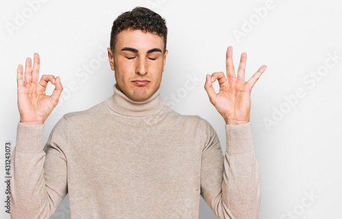 Hispanic young man wearing casual turtleneck sweater relax and smiling with eyes closed doing meditation gesture with fingers. yoga concept.