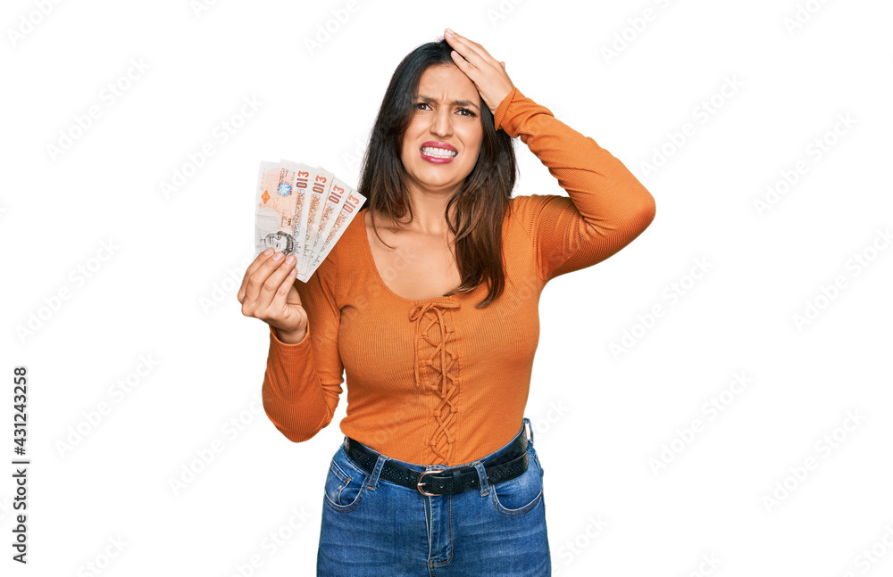 Beautiful hispanic woman holding 10 united kingdom pounds banknotes stressed and frustrated with hand on head, surprised and angry face Beautiful hispanic woman holding 10 united kingdom pounds banknotes stressed and frustrated with hand on head, surprised and angry face