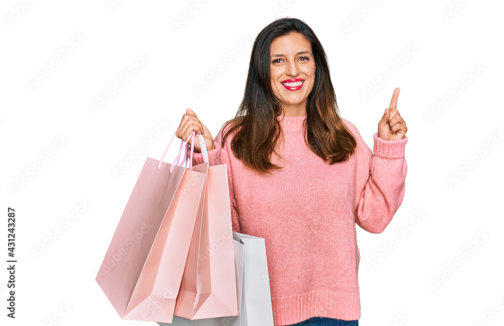 Beautiful hispanic woman holding shopping bags surprised with an idea or question pointing finger with happy face, number one Beautiful hispanic woman holding shopping bags surprised with an idea or question pointing finger with happy face, number one
