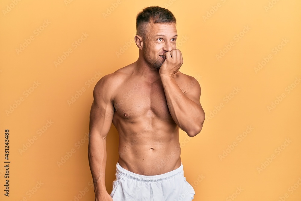 Handsome muscle man standing shirtless looking stressed and nervous with hands on mouth biting nails. anxiety problem.