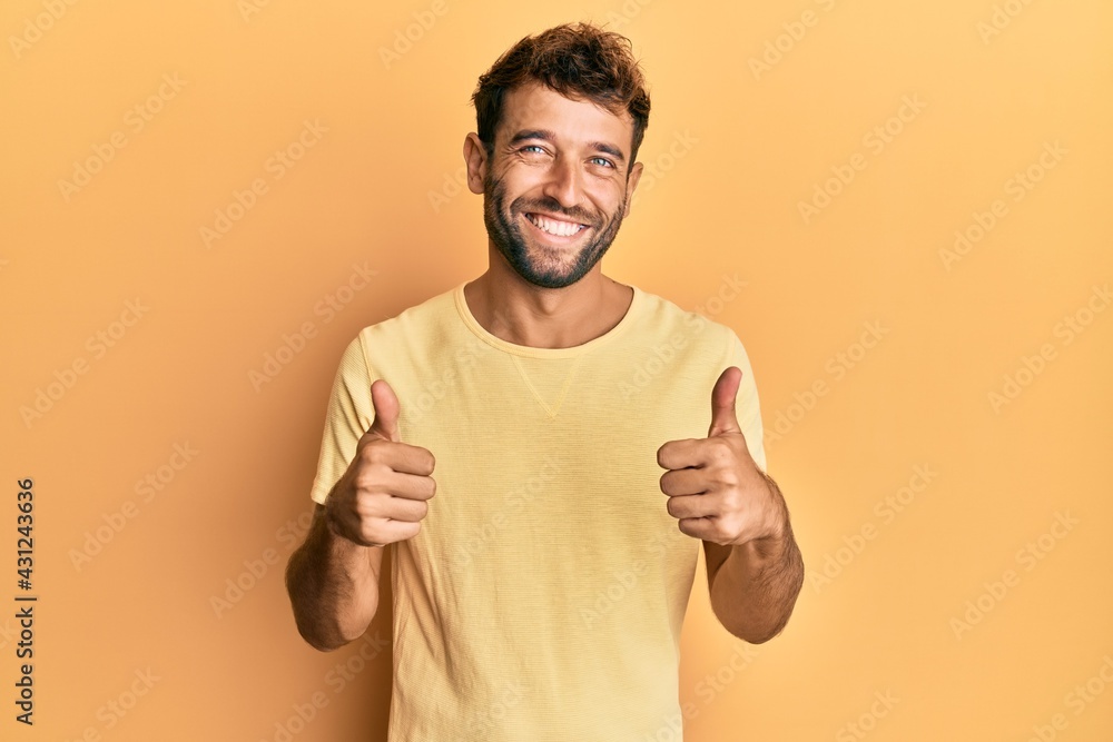 Handsome man with beard wearing casual yellow tshirt over yellow background success sign doing positive gesture with hand, thumbs up smiling and happy. cheerful expression and winner gesture. Handsome man with beard wearing casual yellow tshirt over yellow background success sign doing positive gesture with hand, thumbs up smiling and happy. cheerful expression and winner gesture.