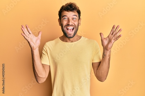 Handsome man with beard wearing casual yellow tshirt over yellow background celebrating crazy and amazed for success with arms raised and open eyes screaming excited. winner concept © Krakenimages.com