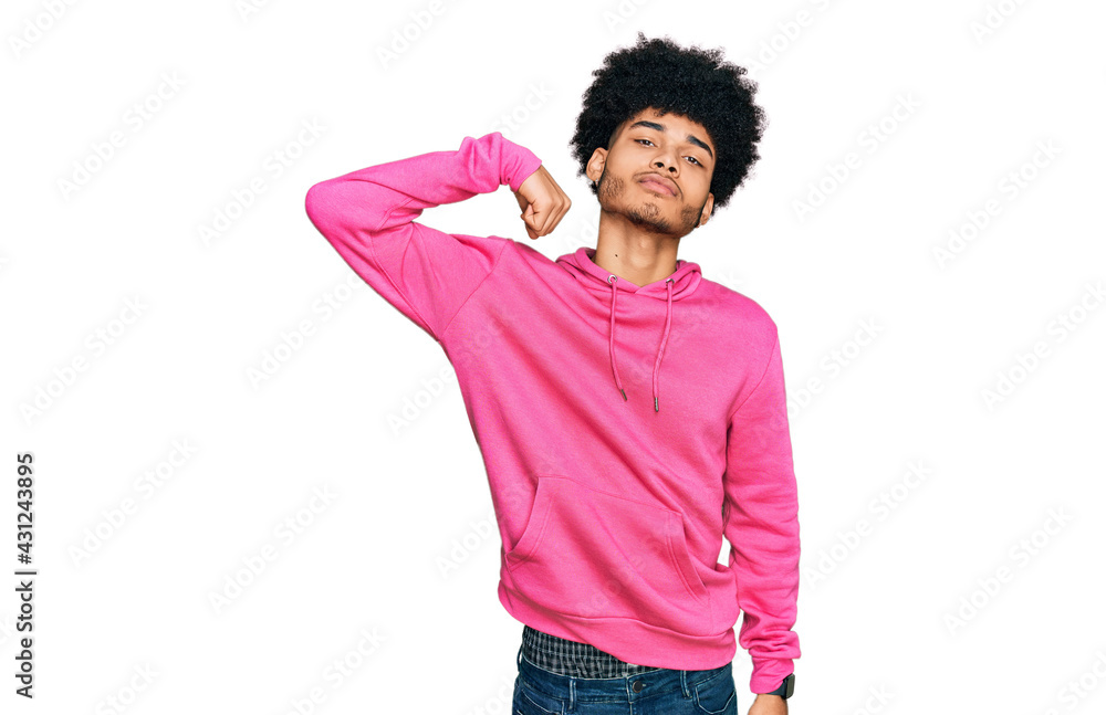 Young african american man with afro hair wearing casual pink sweatshirt strong person showing arm muscle, confident and proud of power Young african american man with afro hair wearing casual pink sweatshirt strong person showing arm muscle, confident and proud of power