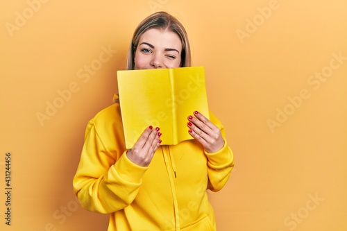 Beautiful caucasian woman holding open book winking looking at the camera with sexy expression, cheerful and happy face.