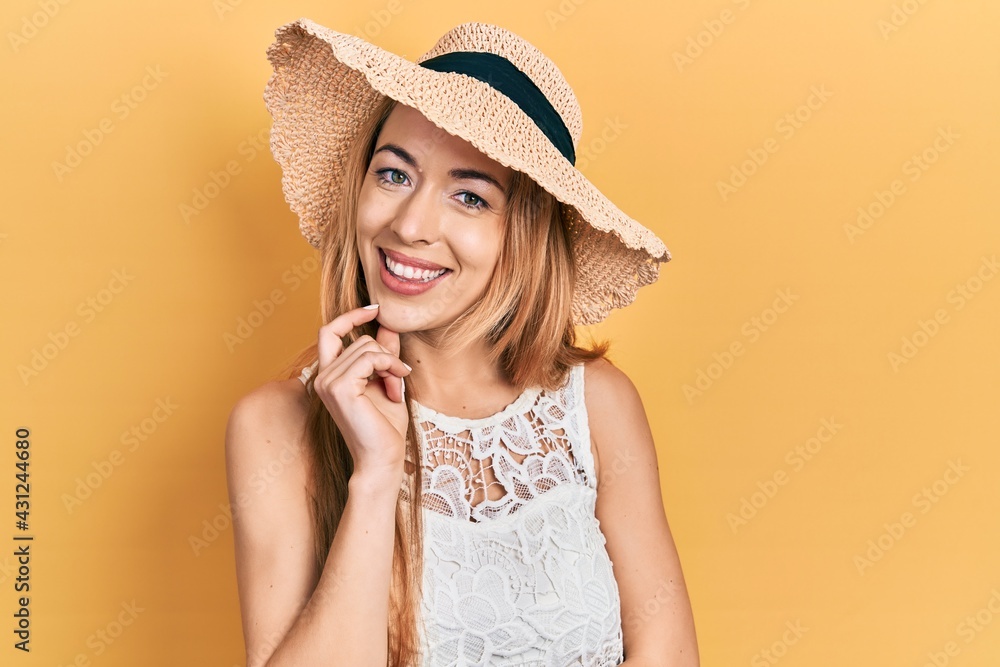 Young caucasian woman wearing summer hat looking confident at the camera with smile with crossed arms and hand raised on chin. thinking positive. Young caucasian woman wearing summer hat looking confident at the camera with smile with crossed arms and hand raised on chin. thinking positive.