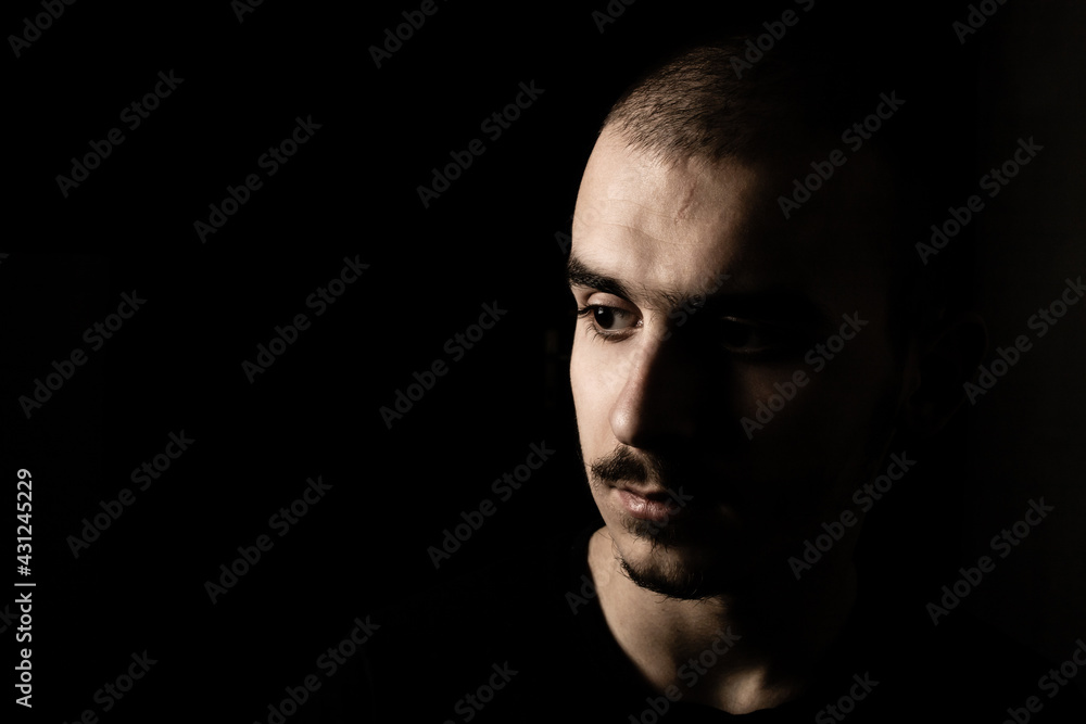 Portrait of a young guy with moustache isolated on black, dark background.
