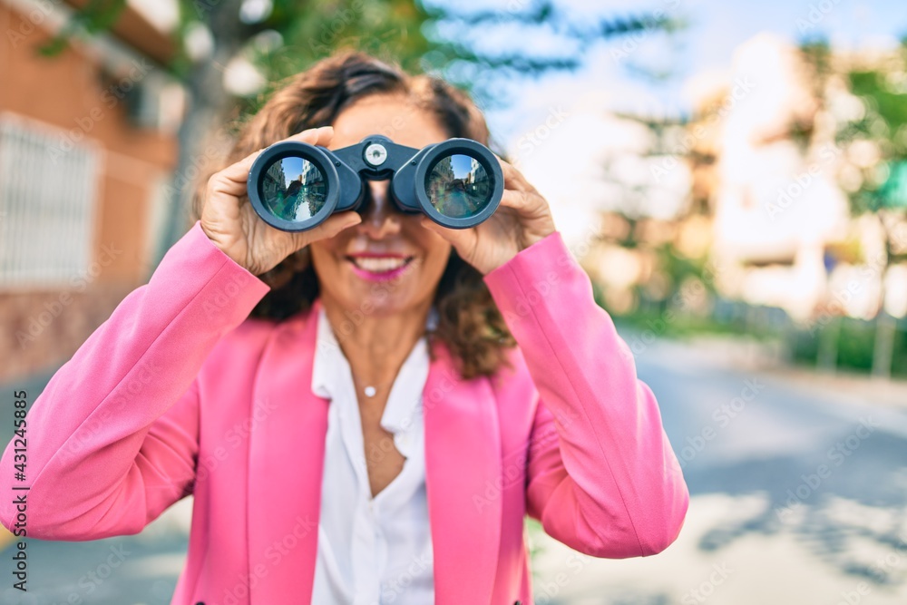 Middle age hispanic businesswoman smiling happy looking for new opportunity using binoculars at the city. Middle age hispanic businesswoman smiling happy looking for new opportunity using binoculars at the city.