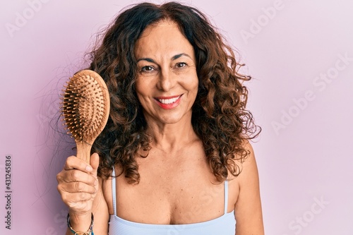 Middle age hispanic woman using comb looking positive and happy standing and smiling with a confident smile showing teeth