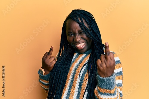 Young black woman with braids wearing casual winter sweater showing middle finger doing fuck you bad expression, provocation and rude attitude. screaming excited