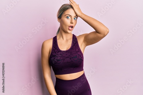 Beautiful blonde woman wearing sportswear over pink background surprised with hand on head for mistake  remember error. forgot  bad memory concept.