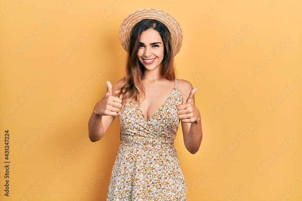 Young hispanic girl wearing summer hat success sign doing positive gesture with hand, thumbs up smiling and happy. cheerful expression and winner gesture. Young hispanic girl wearing summer hat success sign doing positive gesture with hand, thumbs up smiling and happy. cheerful expression and winner gesture.