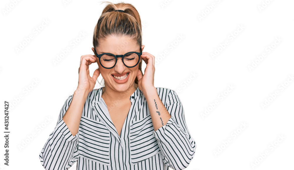 Young caucasian woman wearing business shirt and glasses covering ears with fingers with annoyed expression for the noise of loud music. deaf concept. Young caucasian woman wearing business shirt and glasses covering ears with fingers with annoyed expression for the noise of loud music. deaf concept.