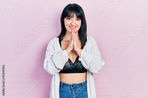 Young hispanic woman wearing lingerie praying with hands together asking for forgiveness smiling confident.