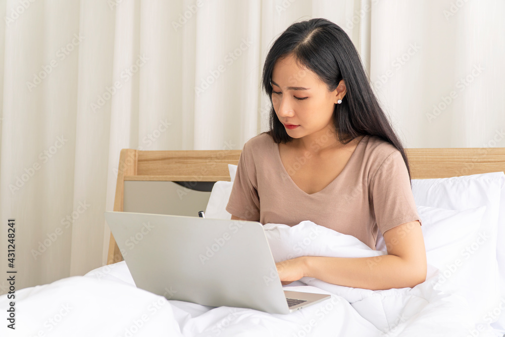 Freelance young woman using laptop working on internet write something on the book while sitting on white bed with pillow in the morning at apartment. Lifestyle work at home with technology concept. Freelance young woman using laptop working on internet write something on the book while sitting on white bed with pillow in the morning at apartment. Lifestyle work at home with technology concept.