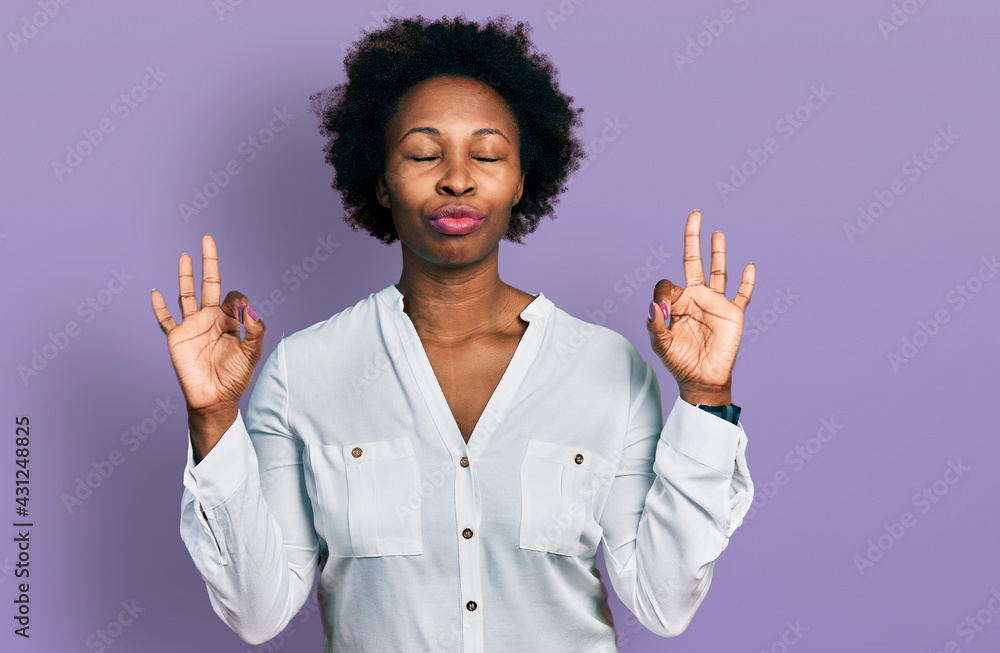 African american woman with afro hair wearing casual white t shirt relax and smiling with eyes closed doing meditation gesture with fingers. yoga concept. African american woman with afro hair wearing casual white t shirt relax and smiling with eyes closed doing meditation gesture with fingers. yoga concept.
