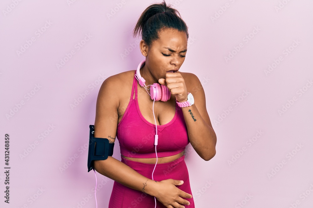 Young african american girl wearing gym clothes and using headphones feeling unwell and coughing as symptom for cold or bronchitis. health care concept. Young african american girl wearing gym clothes and using headphones feeling unwell and coughing as symptom for cold or bronchitis. health care concept.
