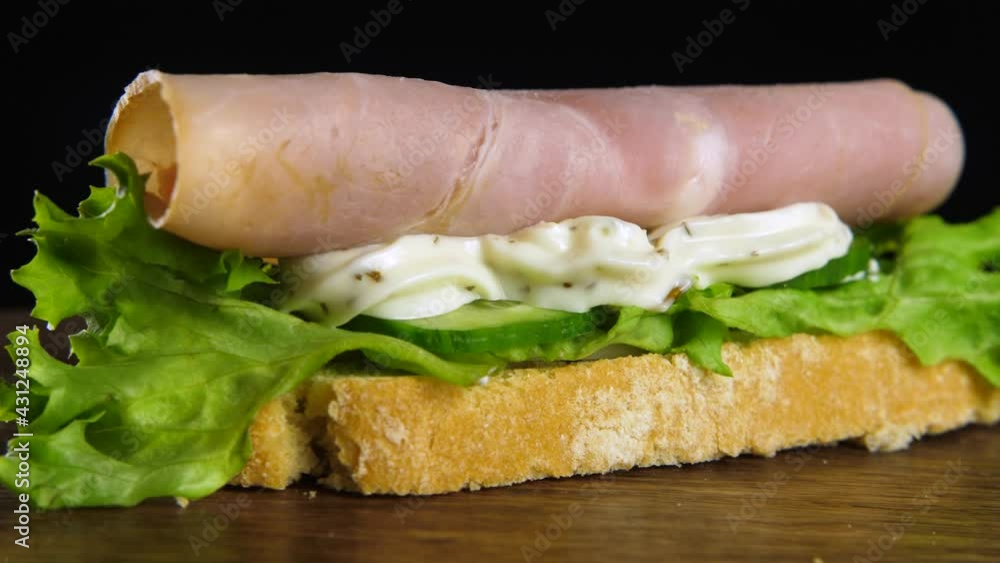 Delicious ciabatta topped with ham, cheese and green lettuce leaves rotating on a black background Delicious ciabatta topped with ham, cheese and green lettuce leaves rotating on a black background