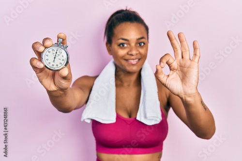 Young african american girl wearing sportswear holding stopwatch doing ok sign with fingers  smiling friendly gesturing excellent symbol