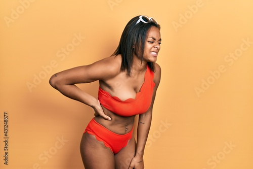 Young african american girl wearing bikini suffering of backache, touching back with hand, muscular pain