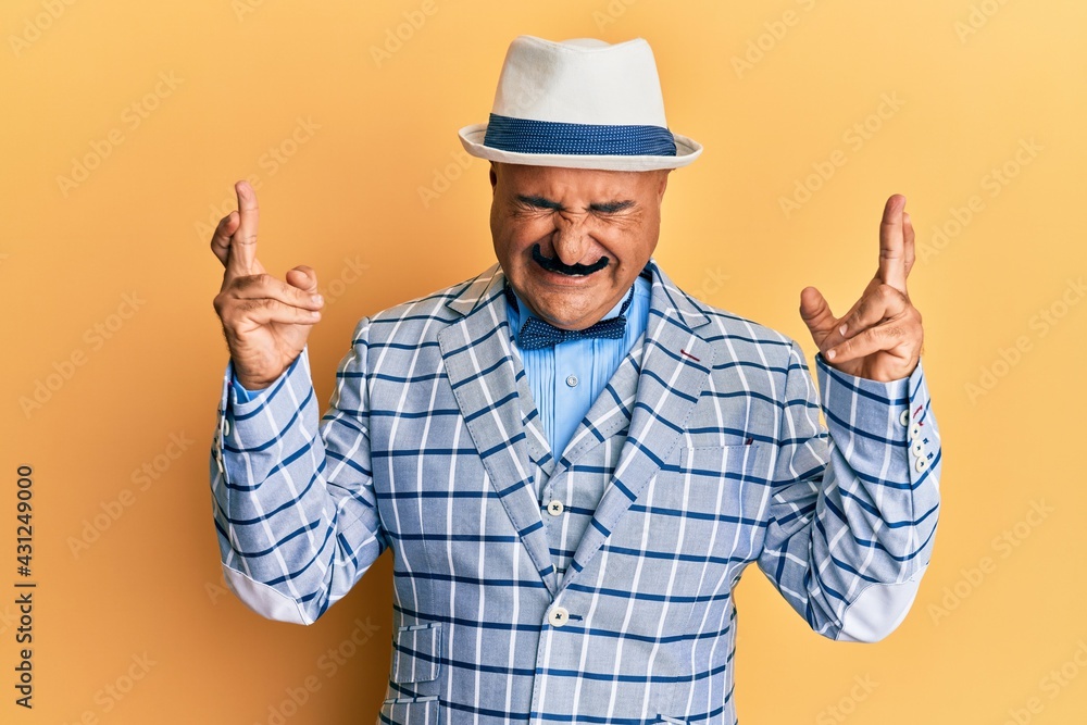 Mature middle east man with mustache wearing vintage and elegant fashion style gesturing finger crossed smiling with hope and eyes closed. luck and superstitious concept.