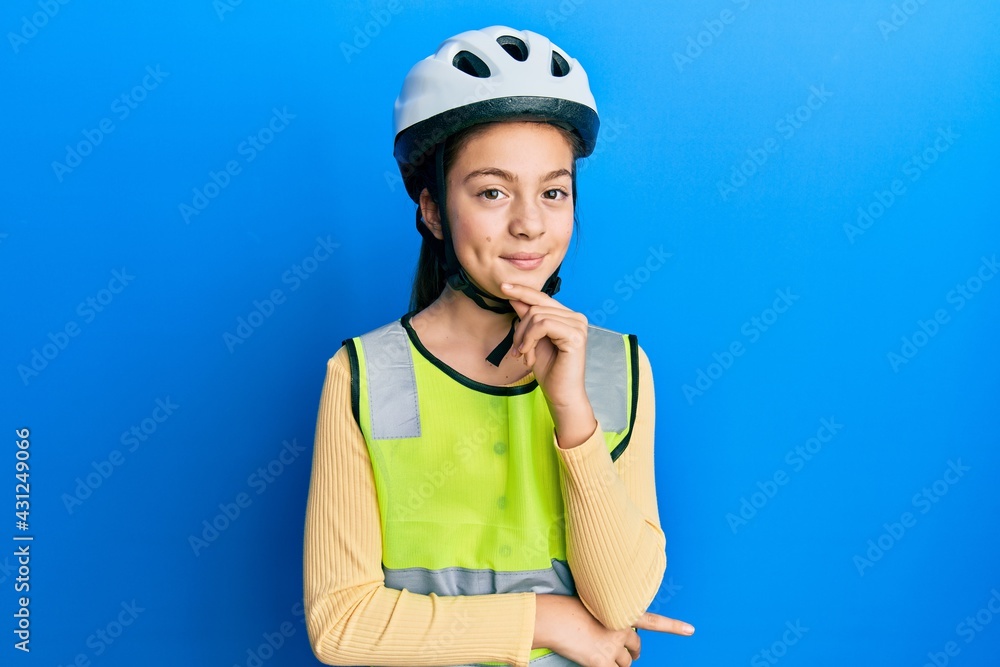 Beautiful brunette little girl wearing bike helmet and reflective vest looking confident at the camera with smile with crossed arms and hand raised on chin. thinking positive. Beautiful brunette little girl wearing bike helmet and reflective vest looking confident at the camera with smile with crossed arms and hand raised on chin. thinking positive.