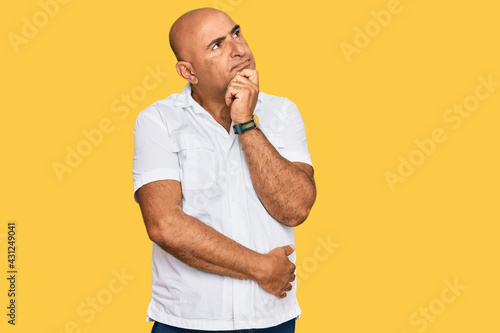 Mature middle east man with mustache wearing casual white shirt with hand on chin thinking about question, pensive expression. smiling with thoughtful face. doubt concept.