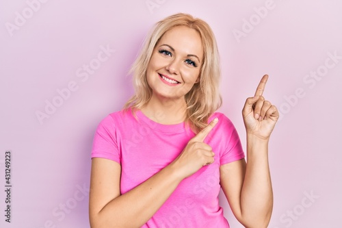 Young blonde woman wearing casual pink t shirt smiling and looking at the camera pointing with two hands and fingers to the side. © Krakenimages.com