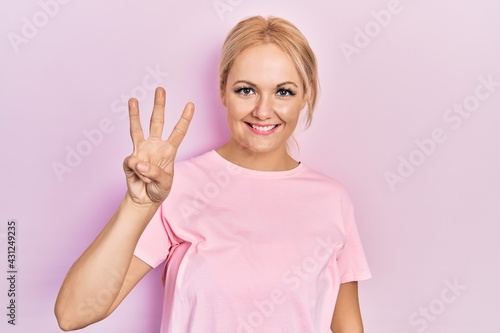 Young blonde woman wearing casual pink t shirt showing and pointing up with fingers number three while smiling confident and happy. © Krakenimages.com
