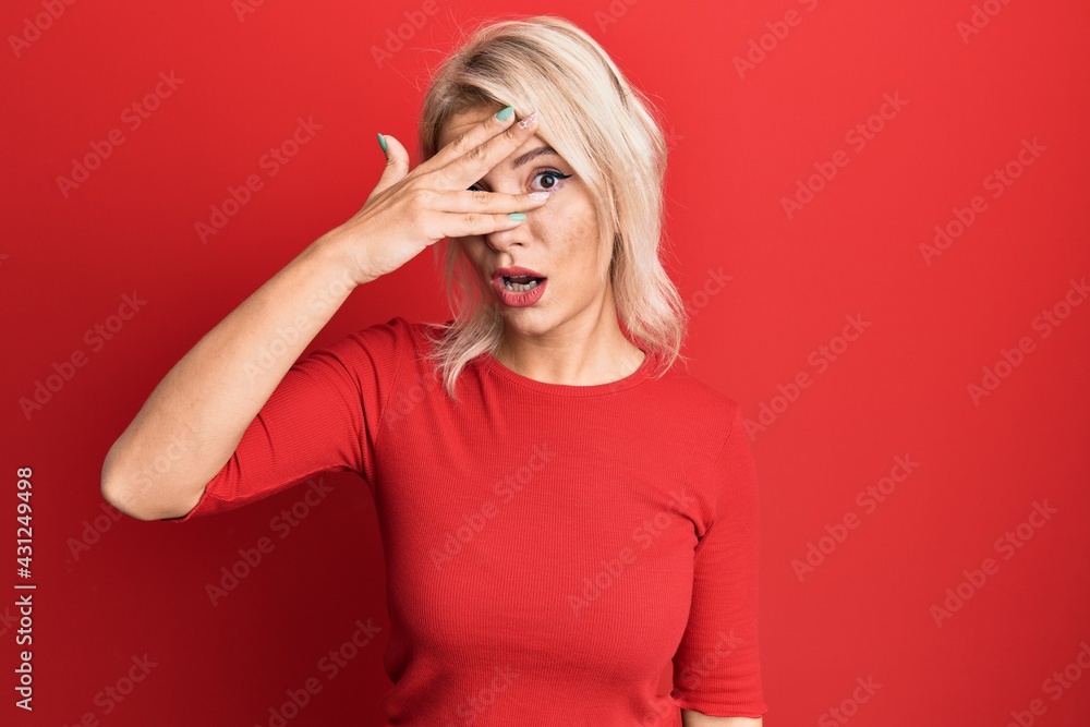 Young blonde girl wearing casual clothes peeking in shock covering face and eyes with hand, looking through fingers with embarrassed expression. Young blonde girl wearing casual clothes peeking in shock covering face and eyes with hand, looking through fingers with embarrassed expression.