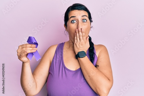 Plus size brunette woman holding purple ribbon awareness covering mouth with hand, shocked and afraid for mistake. surprised expression