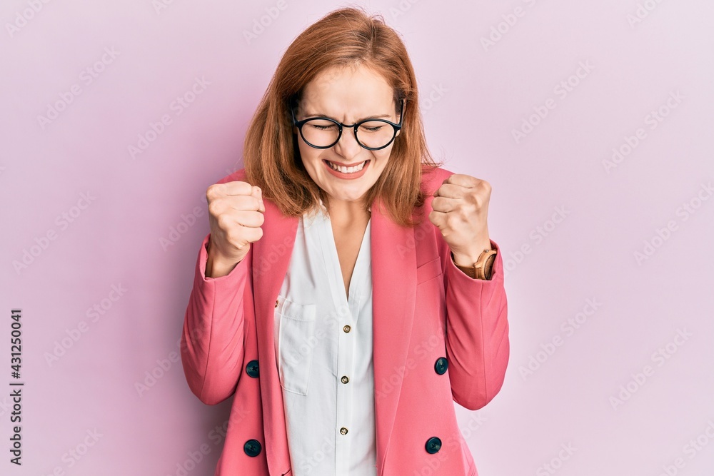 Young caucasian woman wearing business style and glasses excited for success with arms raised and eyes closed celebrating victory smiling. winner concept. Young caucasian woman wearing business style and glasses excited for success with arms raised and eyes closed celebrating victory smiling. winner concept.