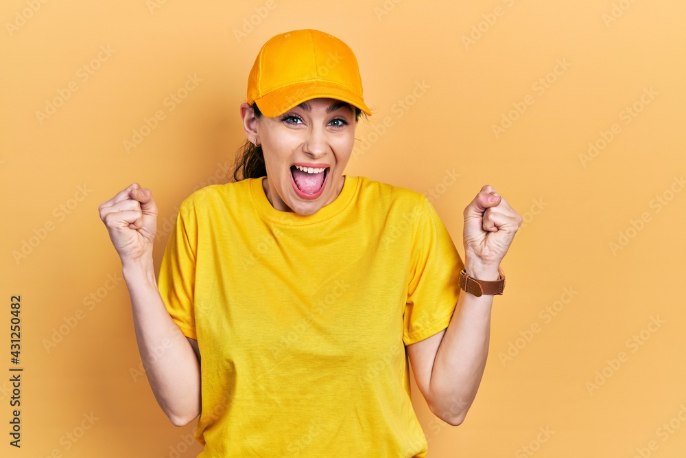 Young hispanic woman wearing delivery uniform and cap celebrating surprised and amazed for success with arms raised and open eyes. winner concept. Young hispanic woman wearing delivery uniform and cap celebrating surprised and amazed for success with arms raised and open eyes. winner concept.