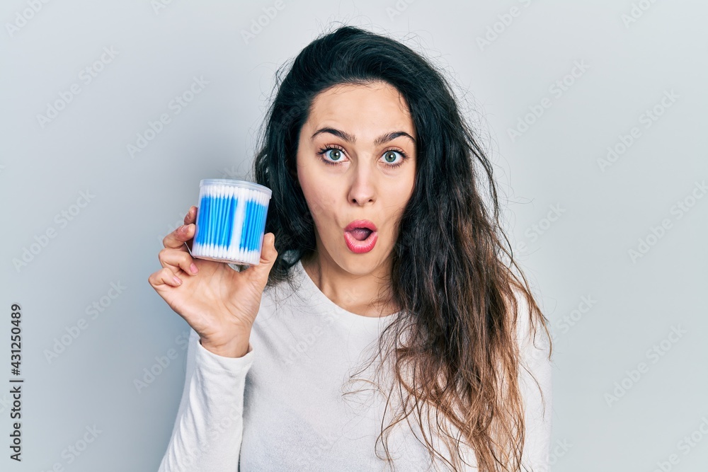 Young hispanic woman holding earwax cotton remover scared and amazed with open mouth for surprise, disbelief face Young hispanic woman holding earwax cotton remover scared and amazed with open mouth for surprise, disbelief face