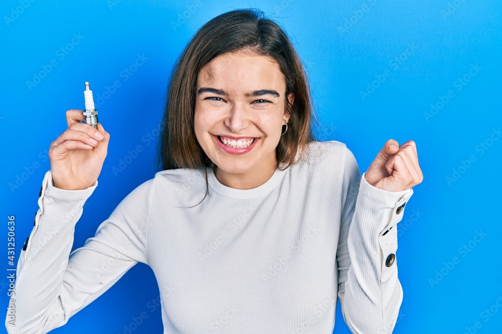 Young caucasian girl holding spark plug screaming proud, celebrating victory and success very excited with raised arm Young caucasian girl holding spark plug screaming proud, celebrating victory and success very excited with raised arm