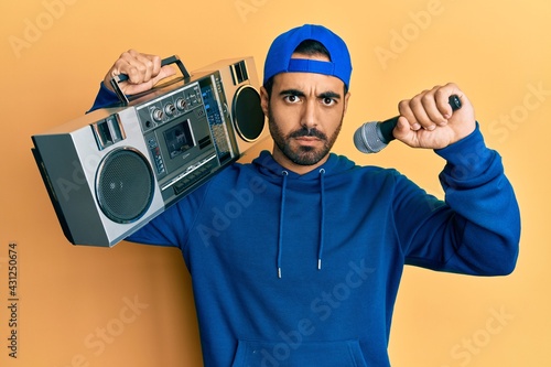 Young hispanic man holding boombox, listening to music singing with microphone skeptic and nervous, frowning upset because of problem. negative person.