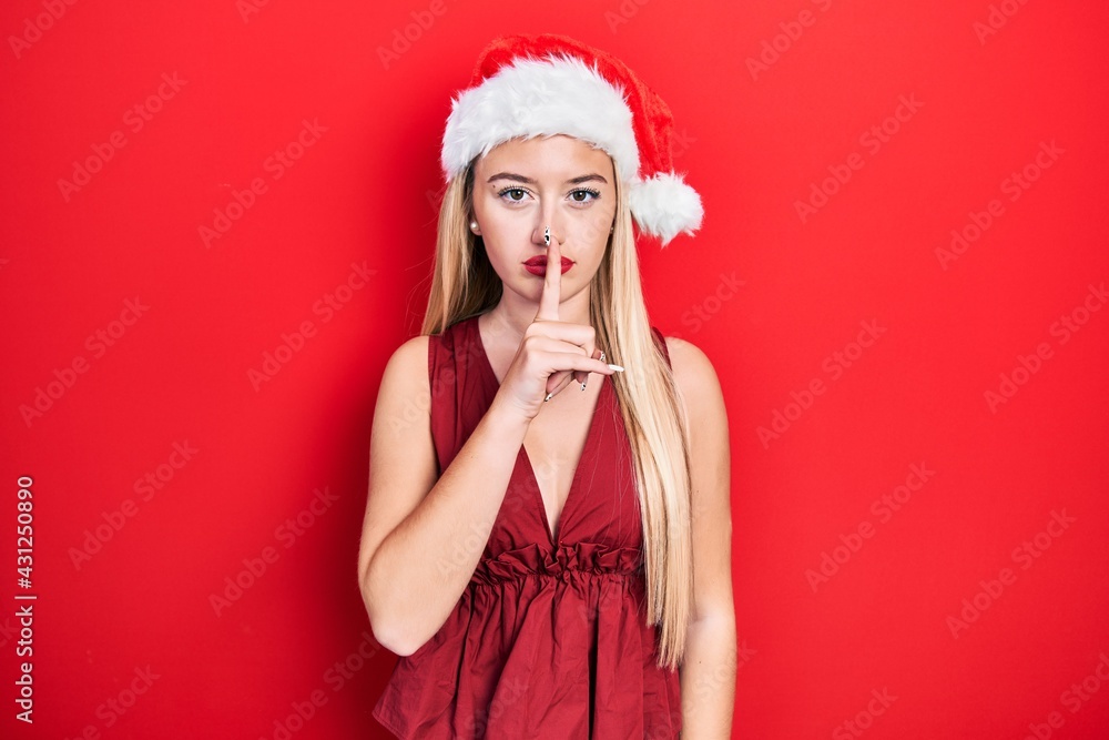 Young blonde girl wearing christmas hat asking to be quiet with finger on lips. silence and secret concept. Young blonde girl wearing christmas hat asking to be quiet with finger on lips. silence and secret concept.