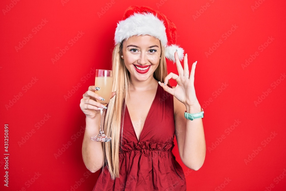 Young blonde girl wearing christmas hat drinking champagne doing ok sign with fingers, smiling friendly gesturing excellent symbol Young blonde girl wearing christmas hat drinking champagne doing ok sign with fingers, smiling friendly gesturing excellent symbol