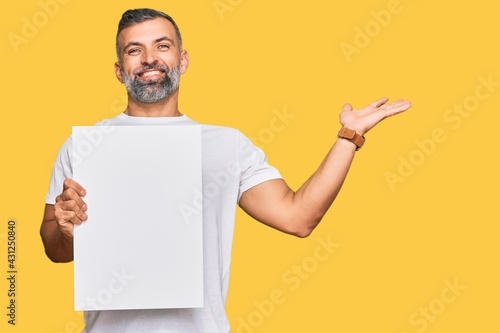 Middle age handsome man holding blank empty banner celebrating victory with happy smile and winner expression with raised hands