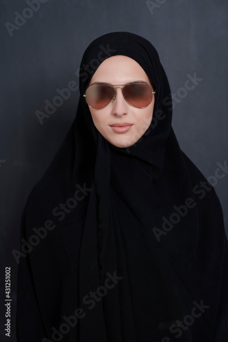 Young muslim businesswoman in traditional clothes or abaya and sunglasses posing in front of black chalkboard