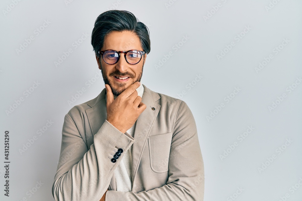 Young hispanic man wearing business jacket and glasses looking confident at the camera smiling with crossed arms and hand raised on chin. thinking positive. Young hispanic man wearing business jacket and glasses looking confident at the camera smiling with crossed arms and hand raised on chin. thinking positive.