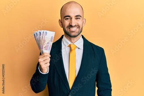 Young hispanic business man holding russian 500 ruble banknotes looking positive and happy standing and smiling with a confident smile showing teeth