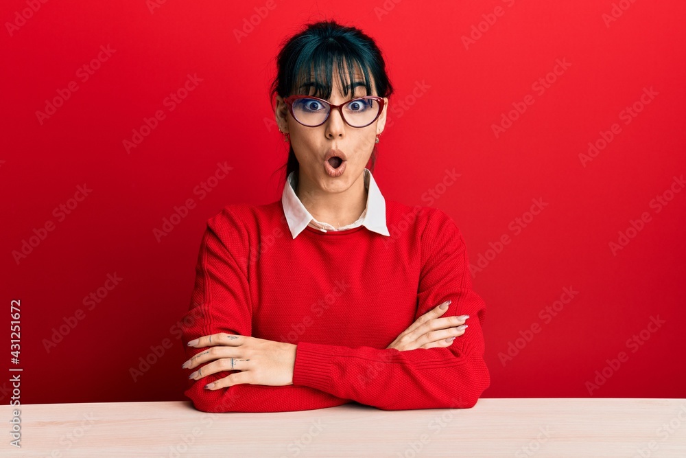 Young brunette woman with bangs wearing glasses sitting on the table afraid and shocked with surprise expression, fear and excited face. Young brunette woman with bangs wearing glasses sitting on the table afraid and shocked with surprise expression, fear and excited face.