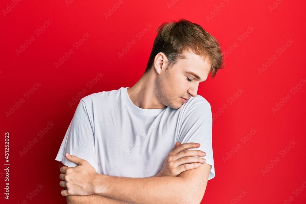 Young caucasian man wearing casual white t shirt hugging oneself happy and positive, smiling confident. self love and self care Young caucasian man wearing casual white t shirt hugging oneself happy and positive, smiling confident. self love and self care
