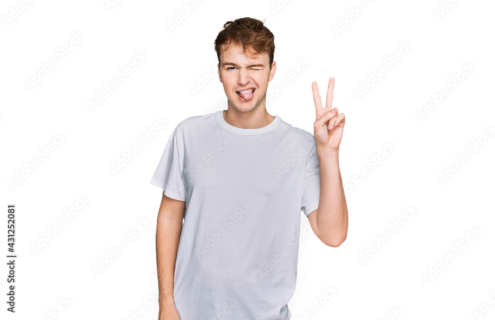 Fototapeta premium Young caucasian man wearing casual white t shirt smiling with happy face winking at the camera doing victory sign. number two.